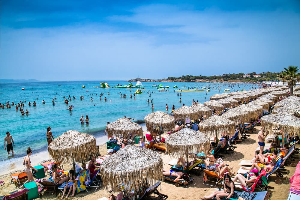 The bustling, cosmopolitan beachfront of Glyfada, with people enjoying the sun near a chic seaside cafe.
