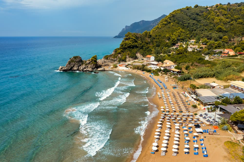 The long, wide stretch of golden sand at Glyfada Beach, Corfu, with stylish sunbeds from a beach club.