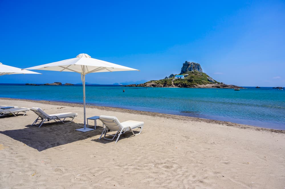 The picturesque Agios Stefanos Beach with ancient ruins on the sand and the Kastri islet in the background.