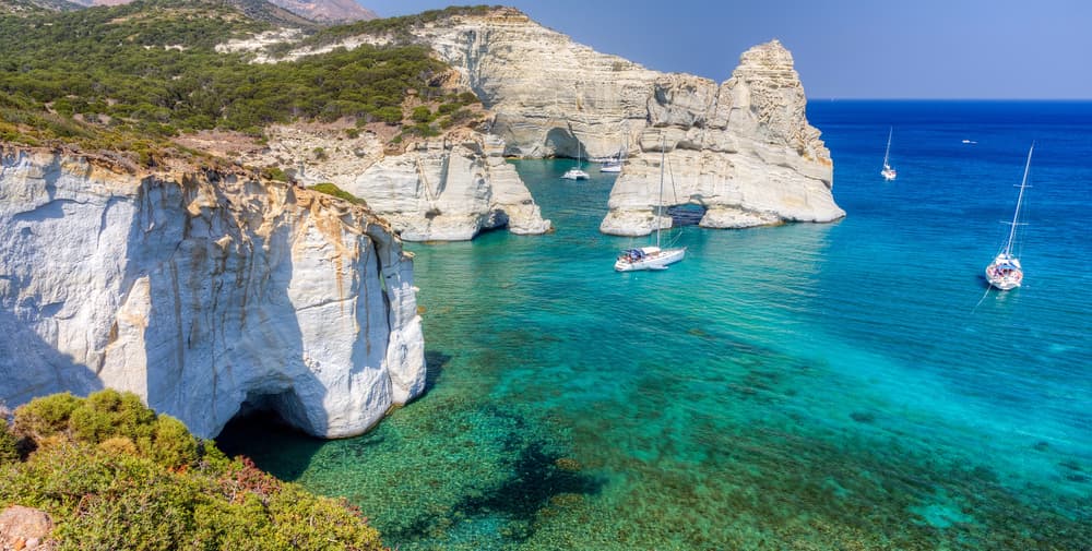 A sailboat anchored in the turquoise waters amidst the towering white sea caves of Kleftiko, Milos.