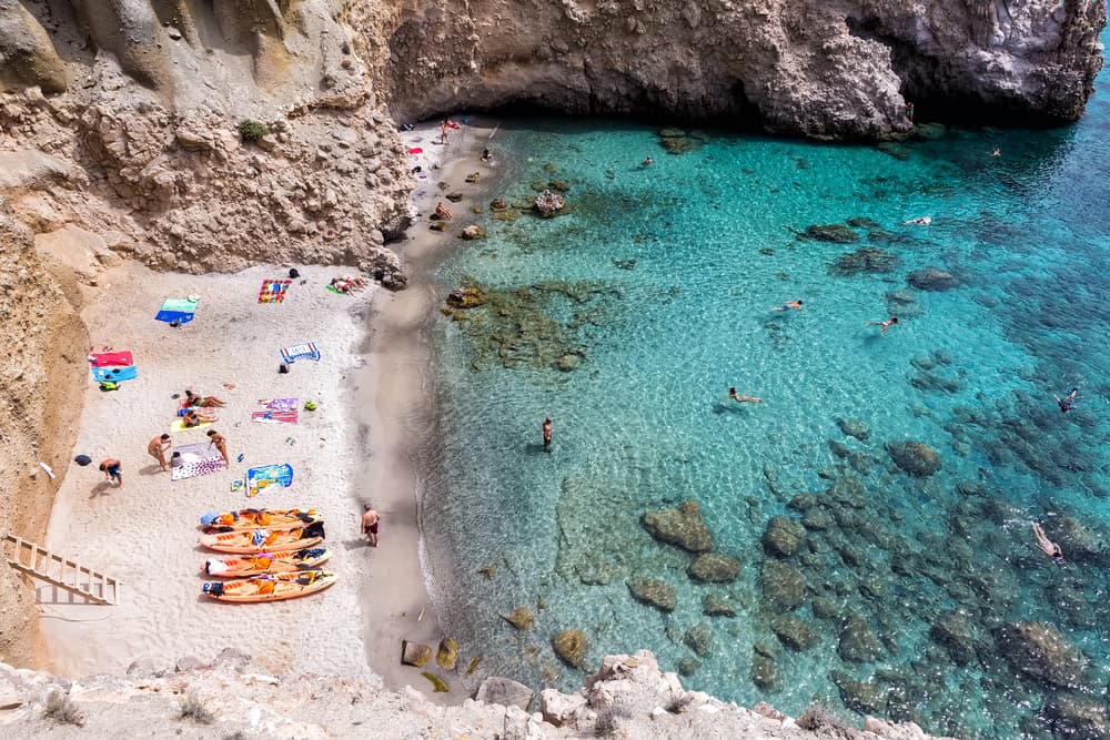 The secluded cove of Tsigrado Beach, with a person carefully descending the rope and ladder.
