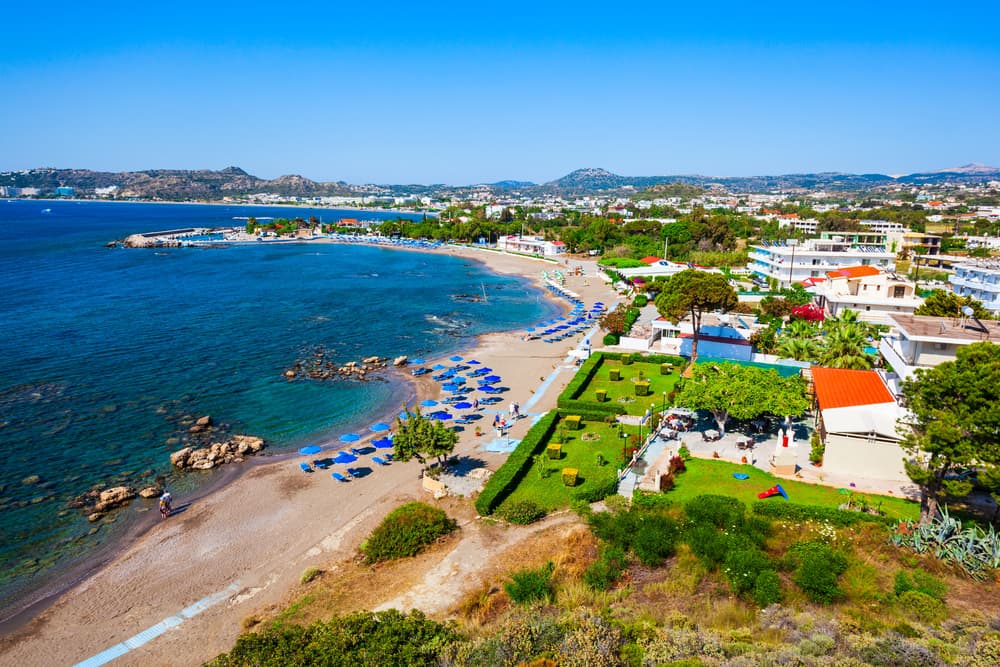 The bustling, organized shoreline of Faliraki Beach, Rhodes, with colorful umbrellas and water sports.