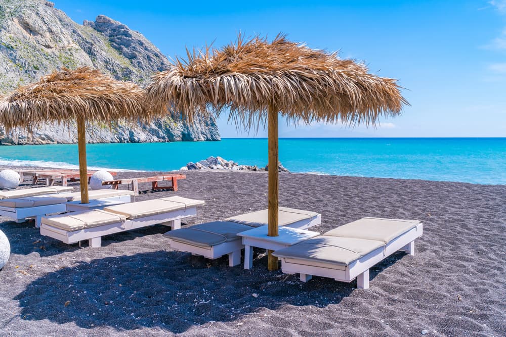 Sunbeds lining the long stretch of black volcanic sand at Perissa Beach, Santorini.